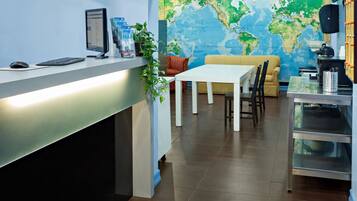 A reception area with a desk, computer, and a large world map mural. There are clocks indicating different cities and a seating area with a table and chairs.
