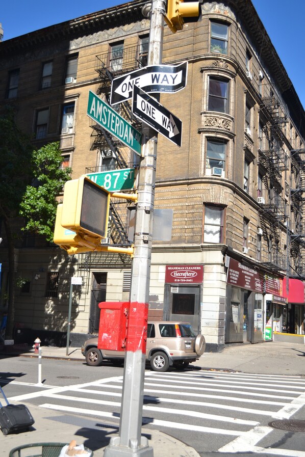 A street corner with a one-way sign, street name signs, and a building with fire escapes.