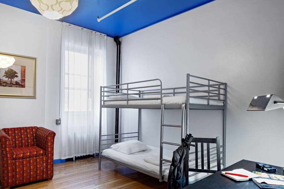 Quarto com beliche, uma cadeira vermelha com padrão, uma escrivaninha com luminária e um quadro na parede.