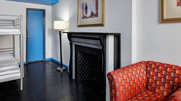 A hotel room with a bunk bed, a fireplace, a patterned armchair, and a framed picture on the wall.