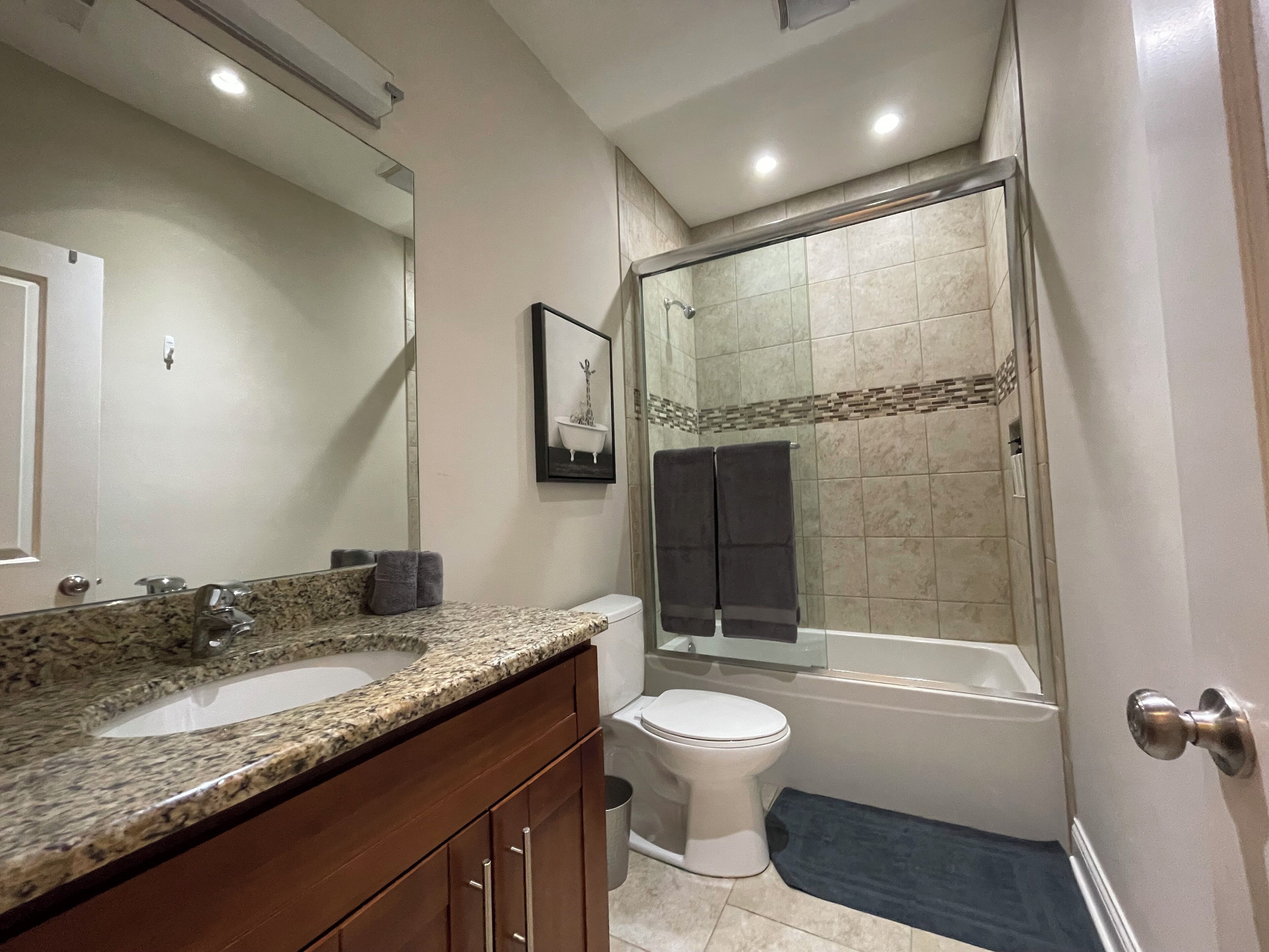 Baño con lavamanos de encimera de granito, inodoro, cabina de ducha con mampara de vidrio y un cuadro en la pared.