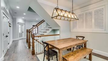 A spacious dining area with a wooden table and bench, a staircase with wooden railings, and a hanging light fixture.