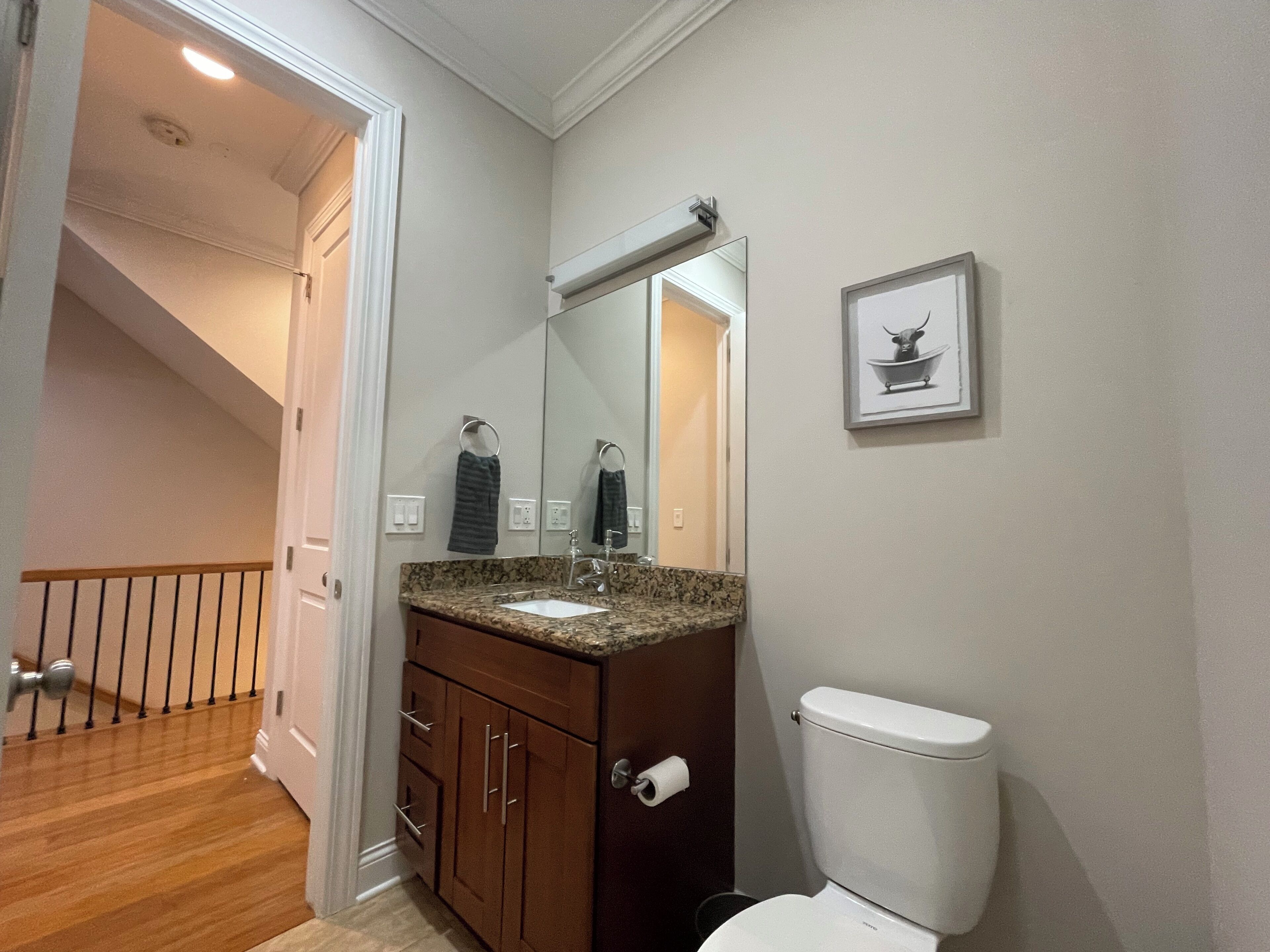 Une salle de bain avec un comptoir en granit, des armoires en bois, des toilettes blanches et un miroir au-dessus du lavabo.