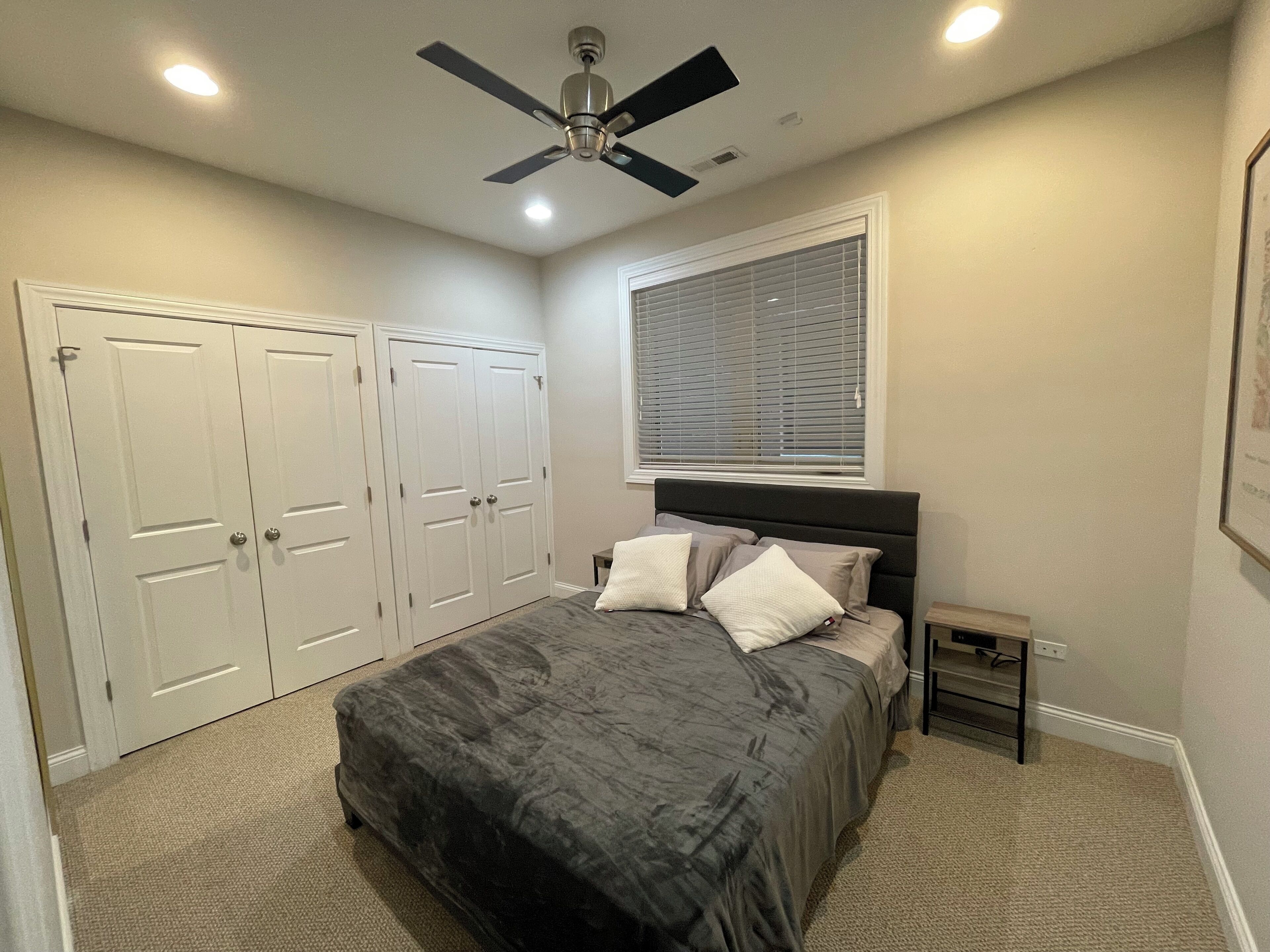 Un dormitorio con cama, ventilador de techo, ventana con persianas y una puerta.