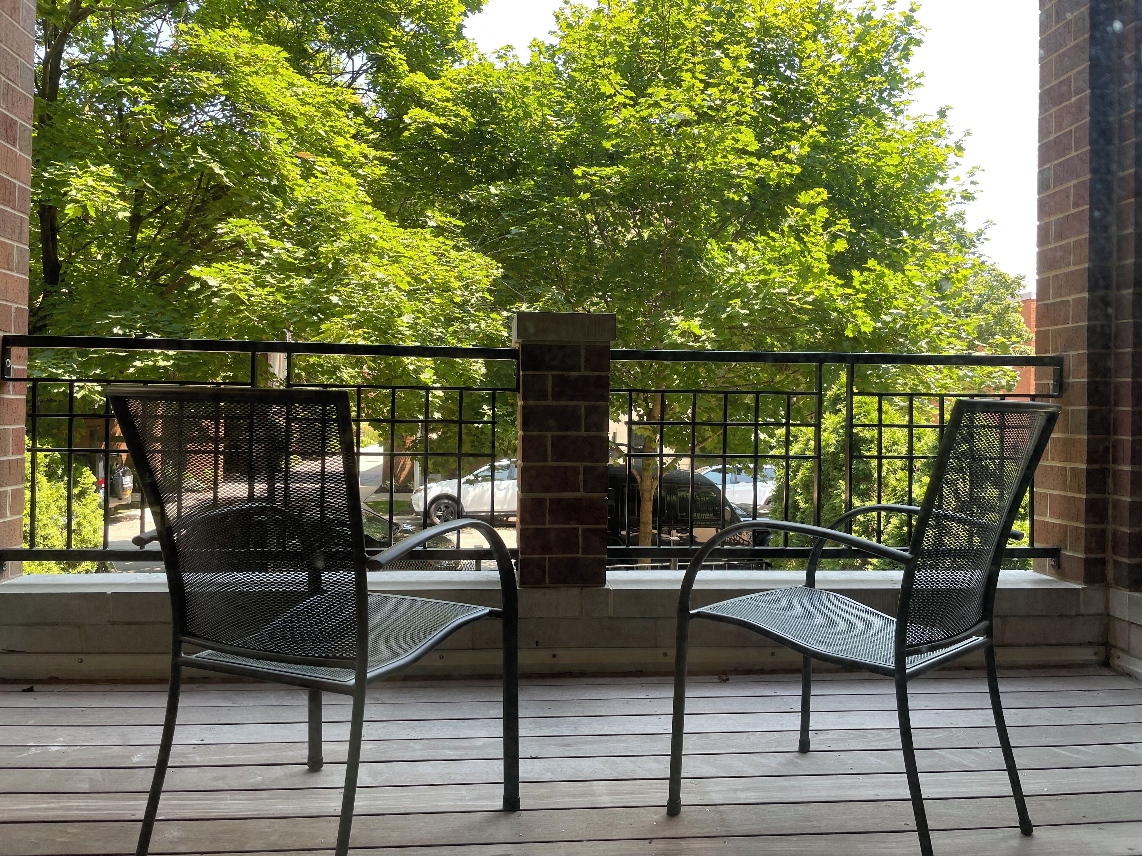 A balcony with two metal chairs and a view of a street with cars and trees.