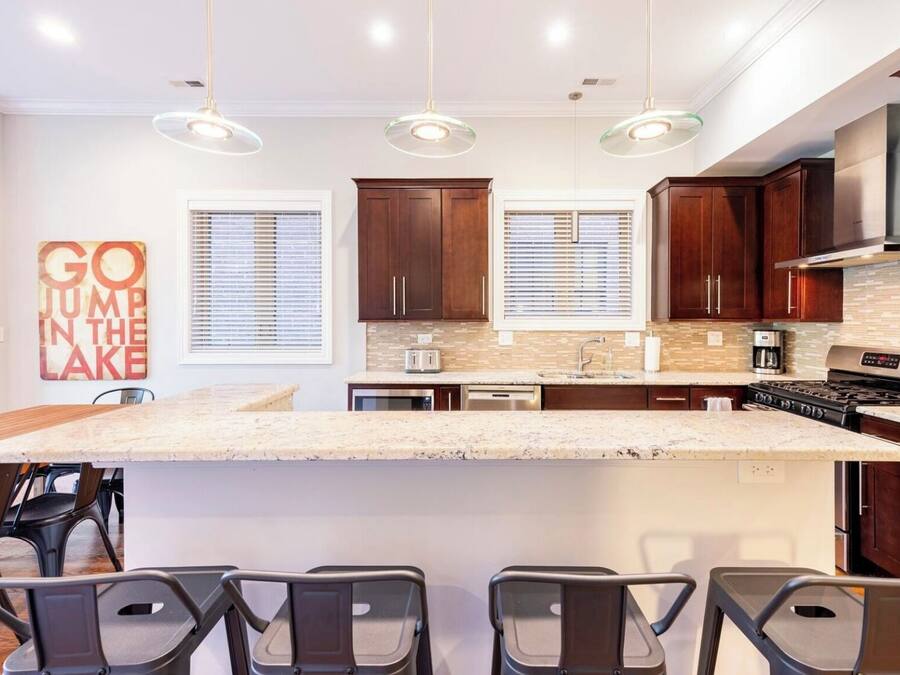 A modern kitchen with a large island, dark wooden cabinets, and pendant lighting.