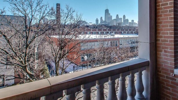 Un balcon offrant une vue sur les toits de la ville, avec notamment un gratte-ciel imposant.