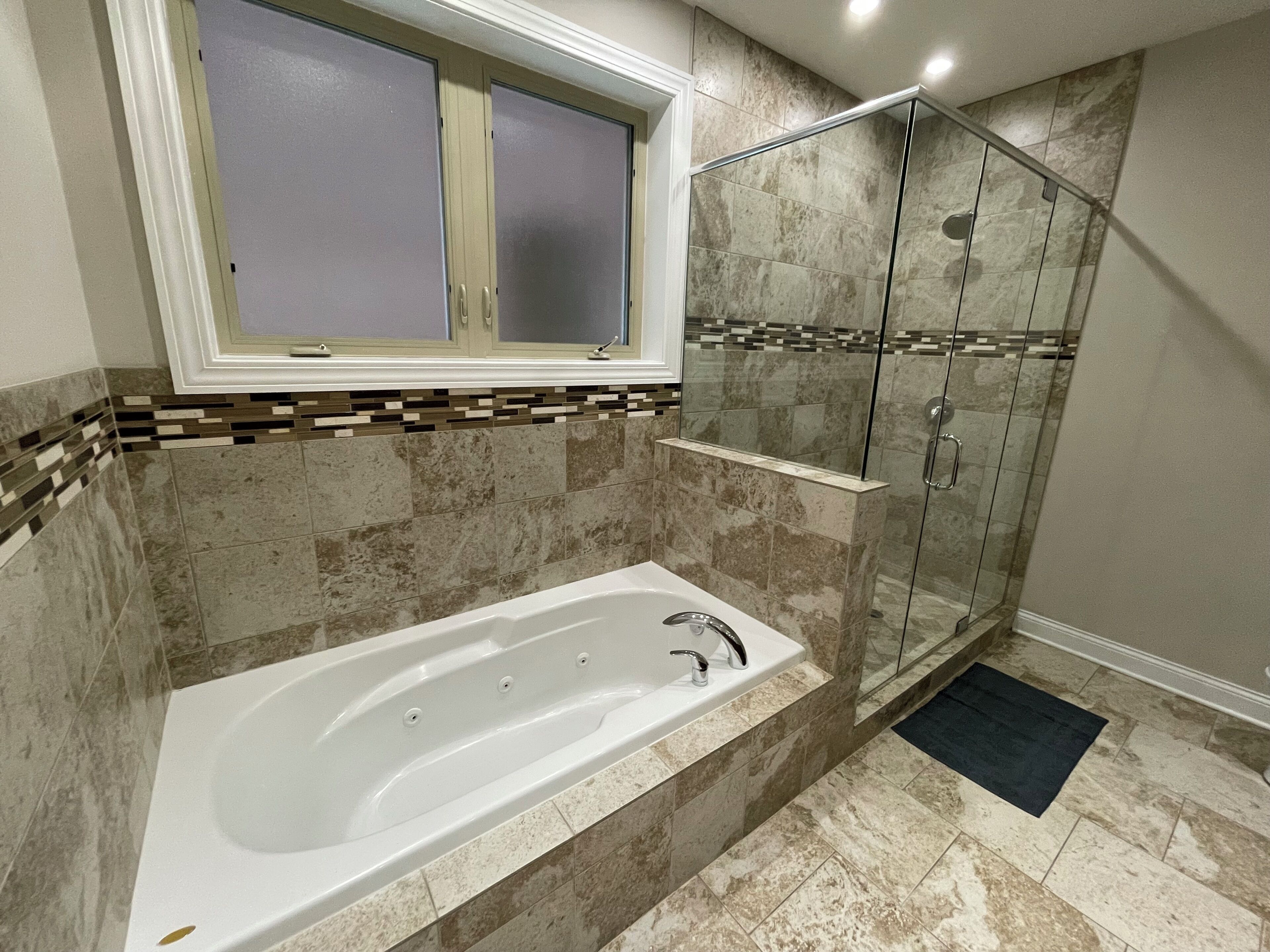 Un baño moderno con una bañera independiente, cabina de ducha con paredes de vidrio y una ventana sobre la bañera.