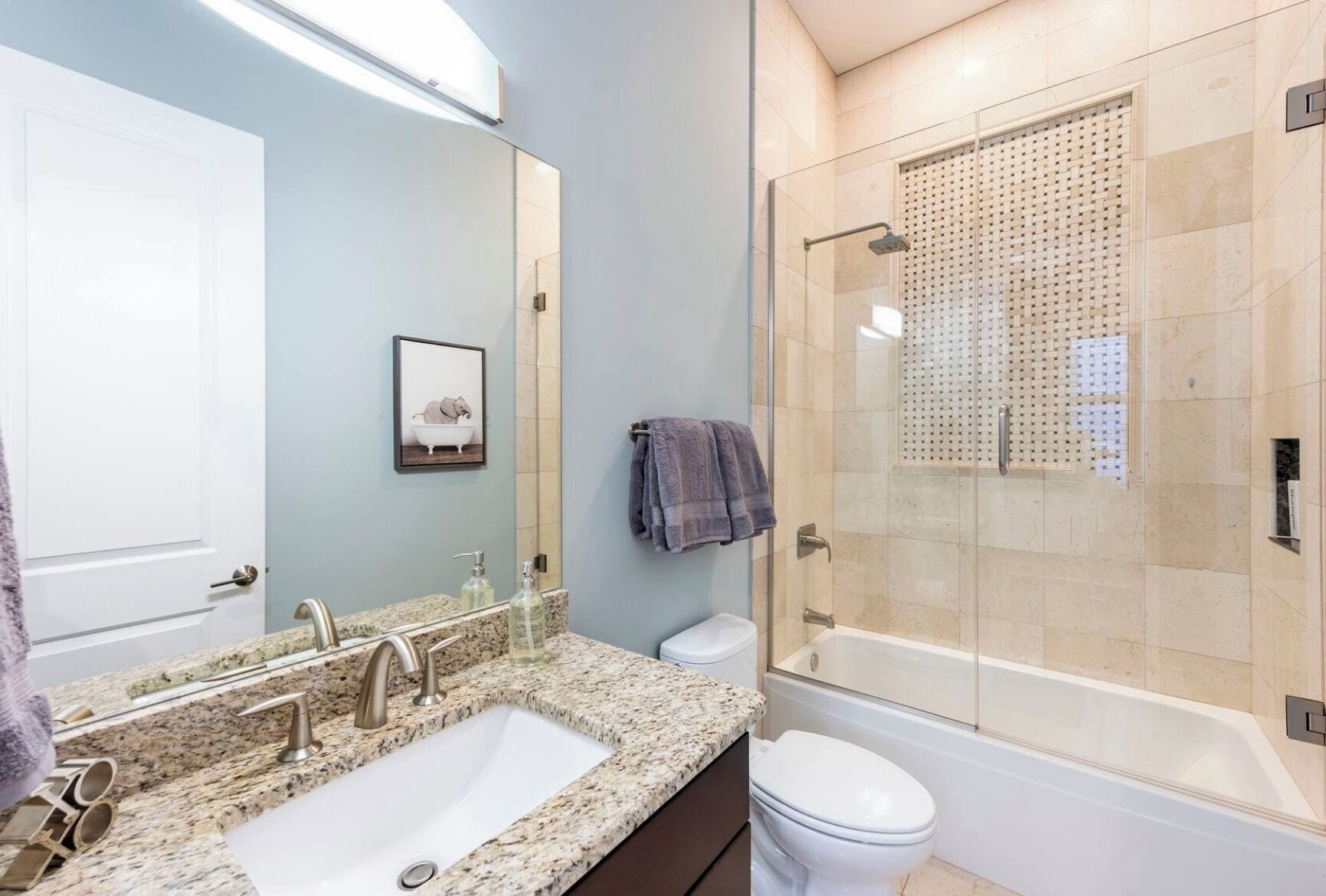 A bathroom with a granite countertop sink, a toilet, and a glass-enclosed shower.
