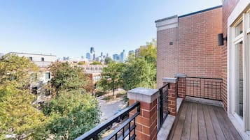 A balcony with a view of a city skyline, brick wall, and a wooden deck.