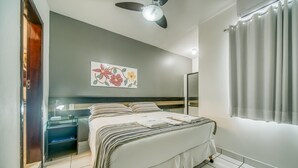 Habitación de hotel moderna con cama, mesitas de noche, ventilador de techo, aire acondicionado instalado en la pared y ventana con cortinas.