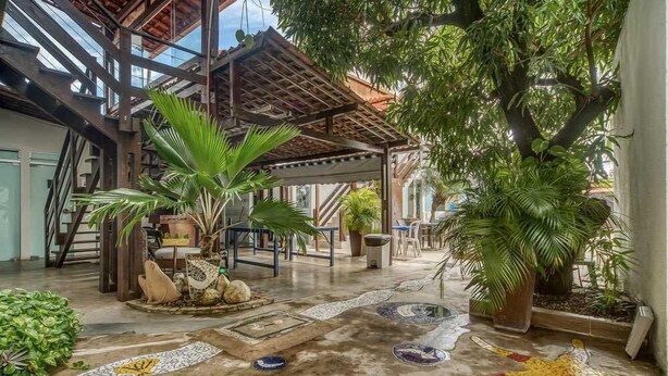 Un patio interior con suelo de baldosas, una pérgola de madera y plantas en macetas.
