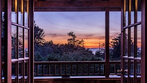 Vue depuis un balcon en bois doté d’une balustrade, donnant sur une zone boisée au coucher du soleil.