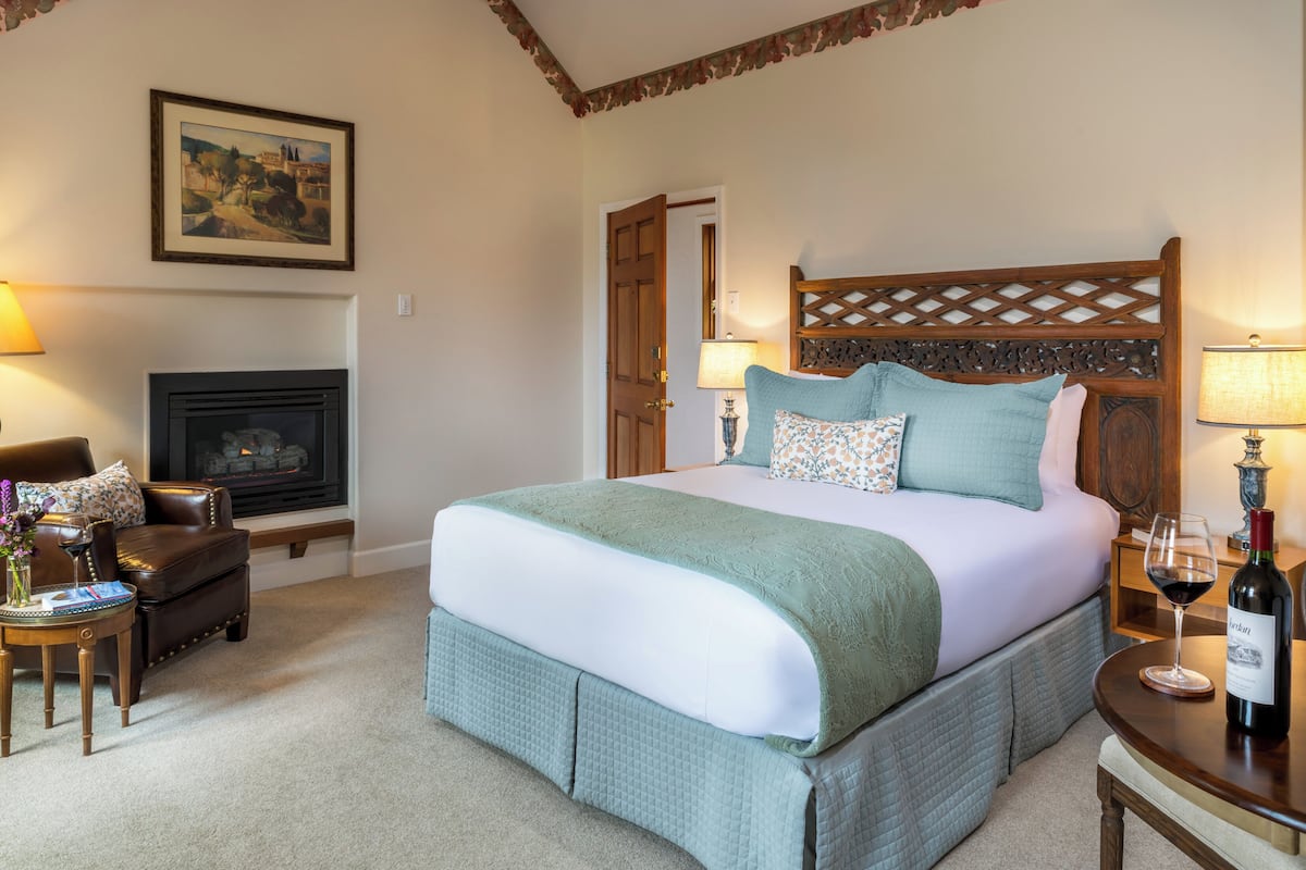 A hotel room with a large bed, a fireplace, a wooden headboard, and a table with a bottle of wine.