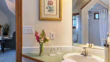 Une salle de bain avec un lavabo, un miroir et une douche. Un tableau botanique encadré orne le mur, et un vase rempli de fleurs est posé sur le comptoir.