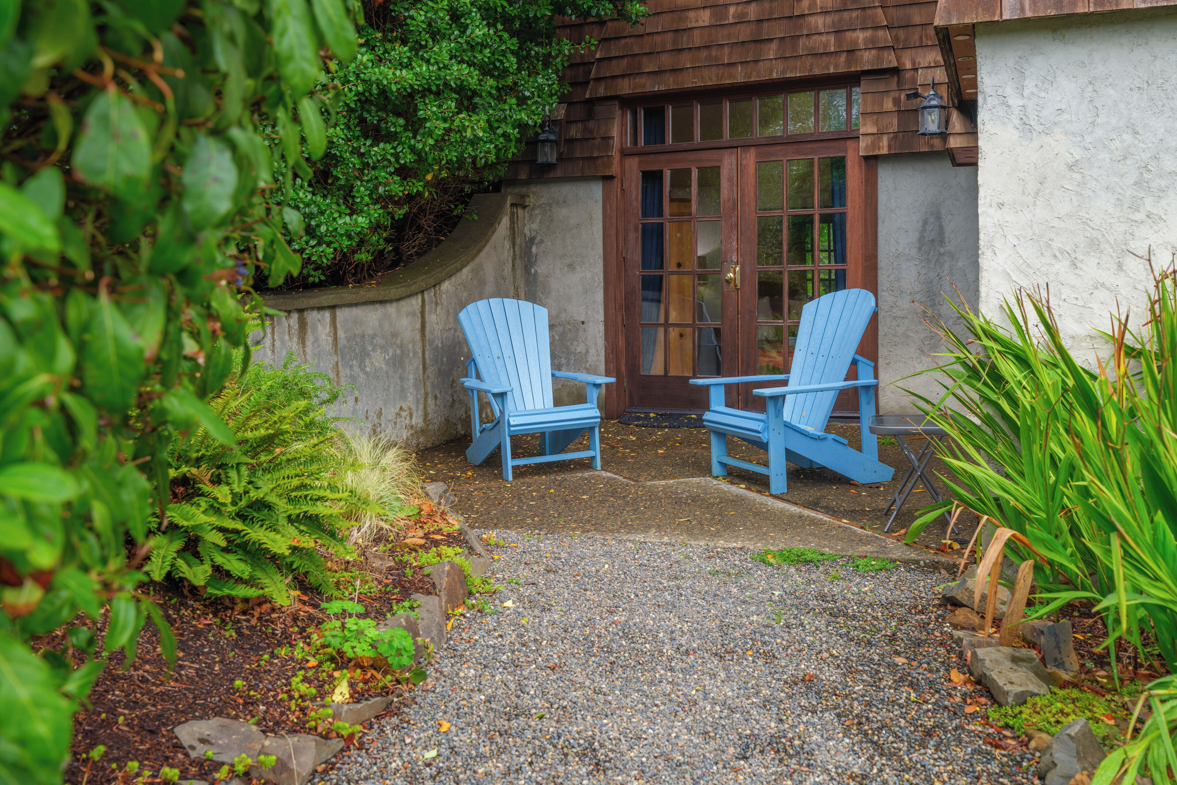 Eine gepflasterte Terrasse mit zwei blauen Adirondack-Stühlen und einer Holztür.