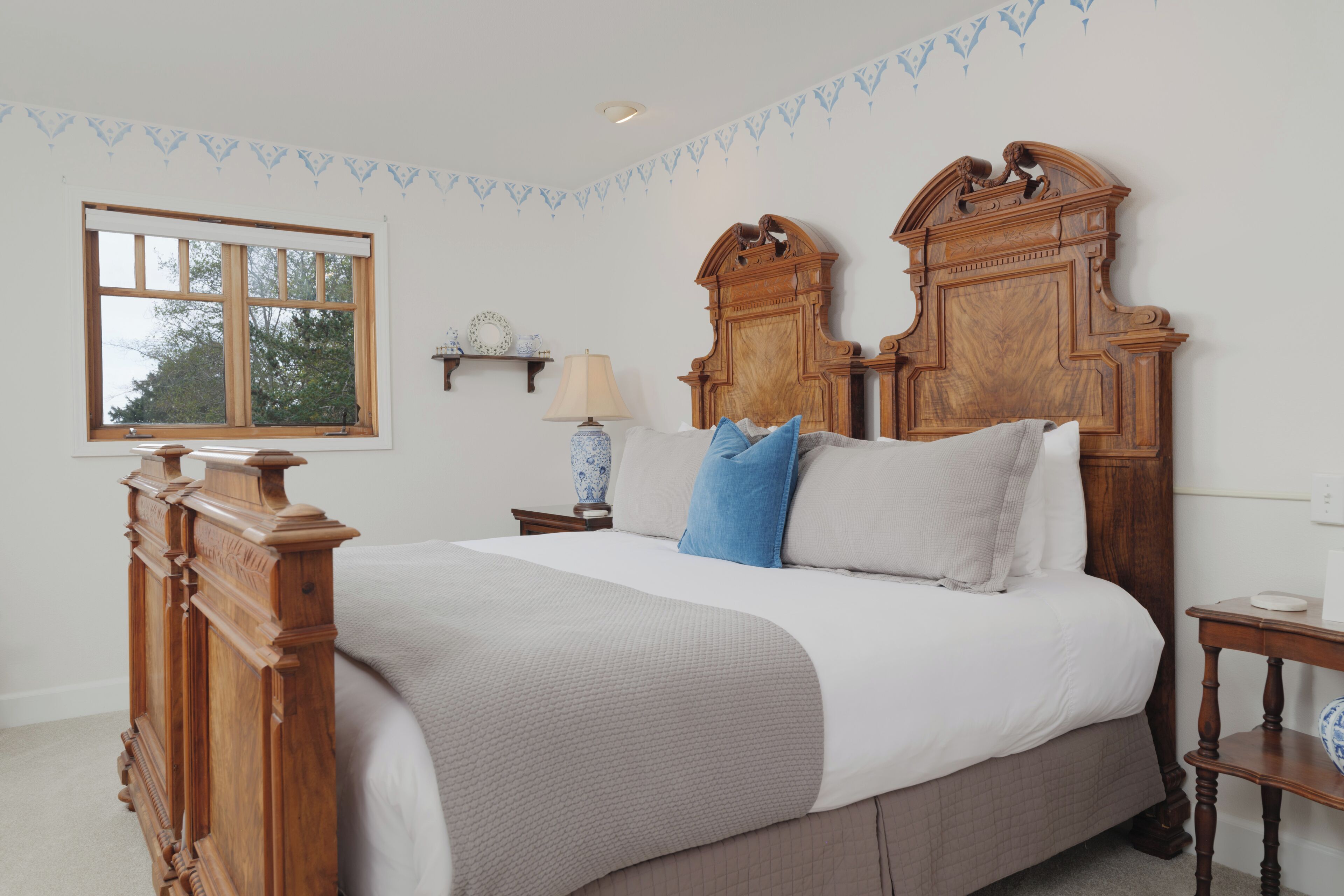 Quarto com uma cama grande, cabeceira de madeira, mesa de cabeceira com abajur e uma janela.