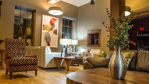 A modern living room with a wooden floor, a patterned armchair, a sofa, a coffee table, and a decorative vase. - Jackson Park Inn, an Ascend Collection Hotel (Pulaski)