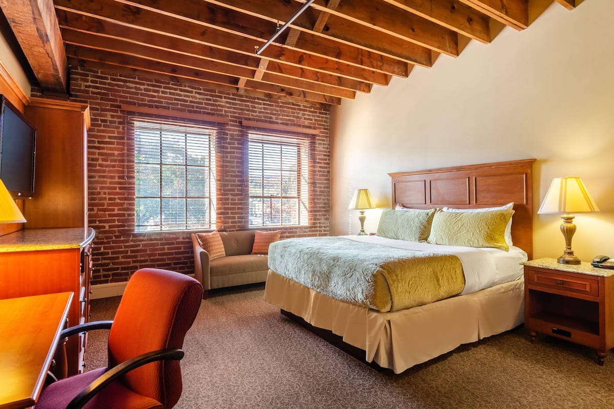 A bedroom with a large bed, a desk with a chair, a sofa, and a TV on a wooden cabinet.