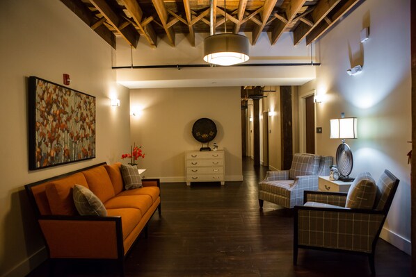 A living room with a sofa, armchairs, a coffee table, a side table, and a lamp. There is a painting on the wall and a decorative plate on a dresser. - Jackson Park Inn, an Ascend Collection Hotel (Pulaski)