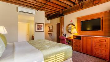A bedroom with a bed, wooden ceiling beams, a TV, a desk, and a chair.