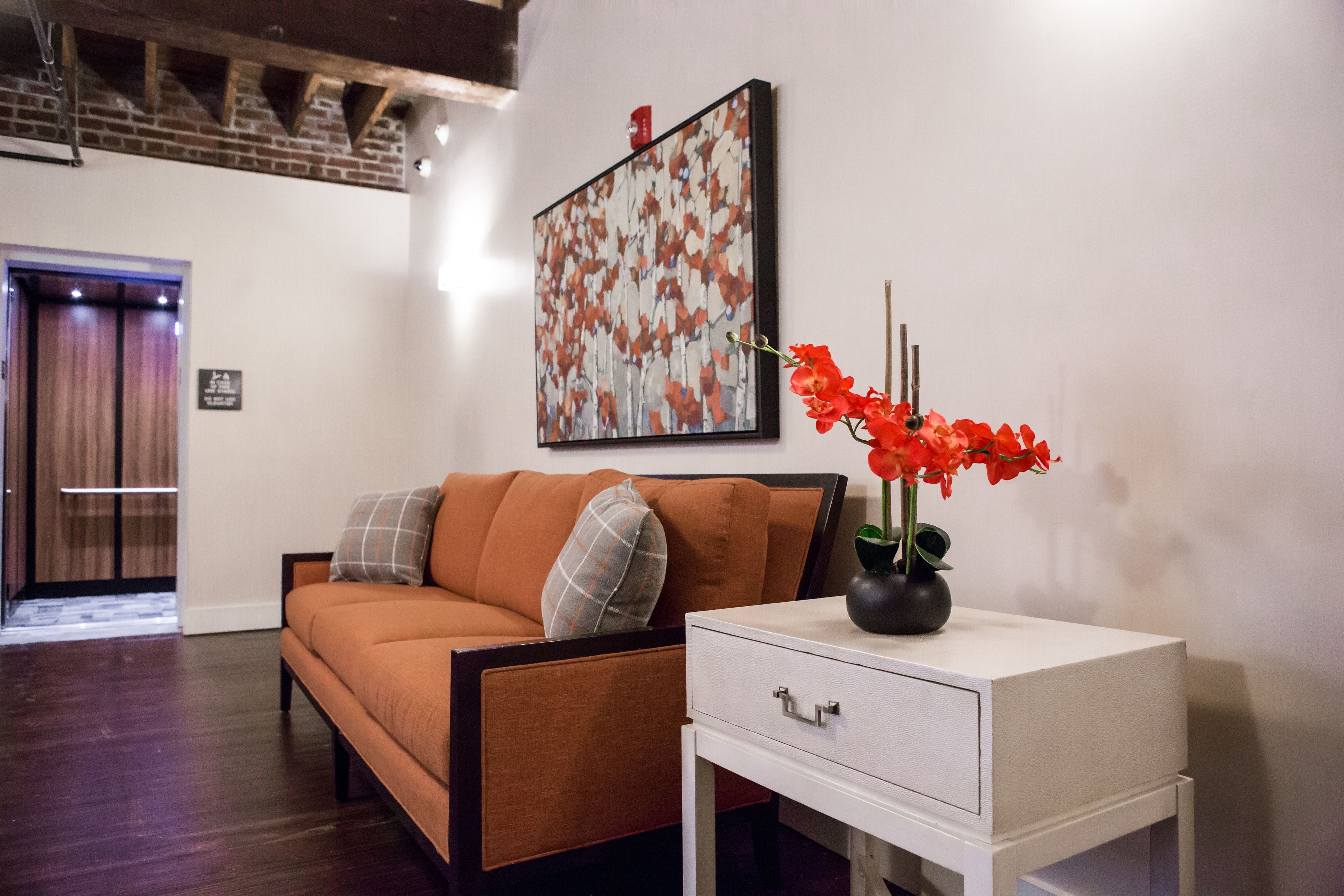 A modern living room with a brown sofa, a white side table, and a framed abstract painting on the wall.