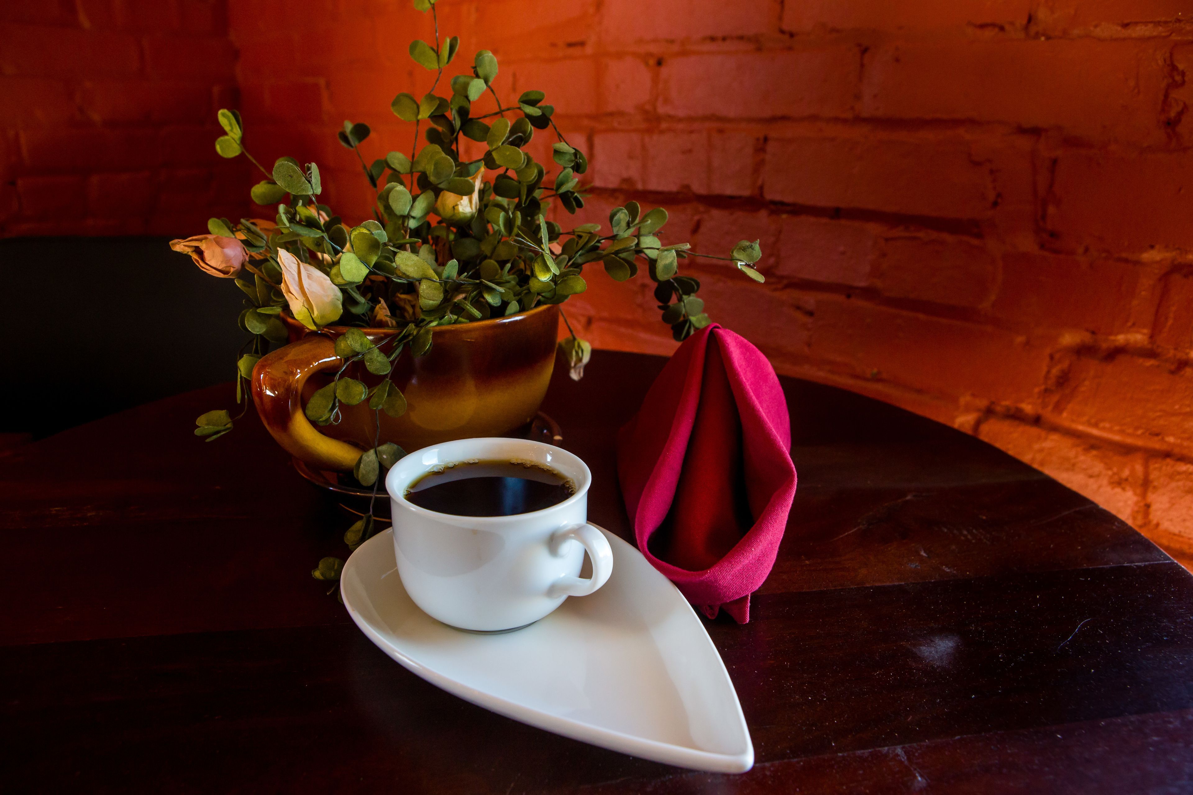 Una mesa con una taza de café, una planta en maceta y un paño rojo.