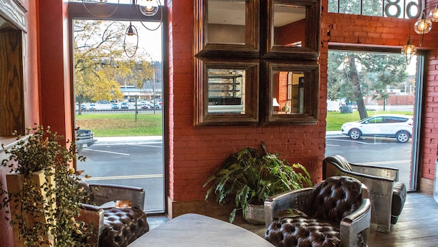 A cozy interior with a leather sofa, a wooden table, and a view of the street through large windows. - Jackson Park Inn, an Ascend Collection Hotel (Pulaski)