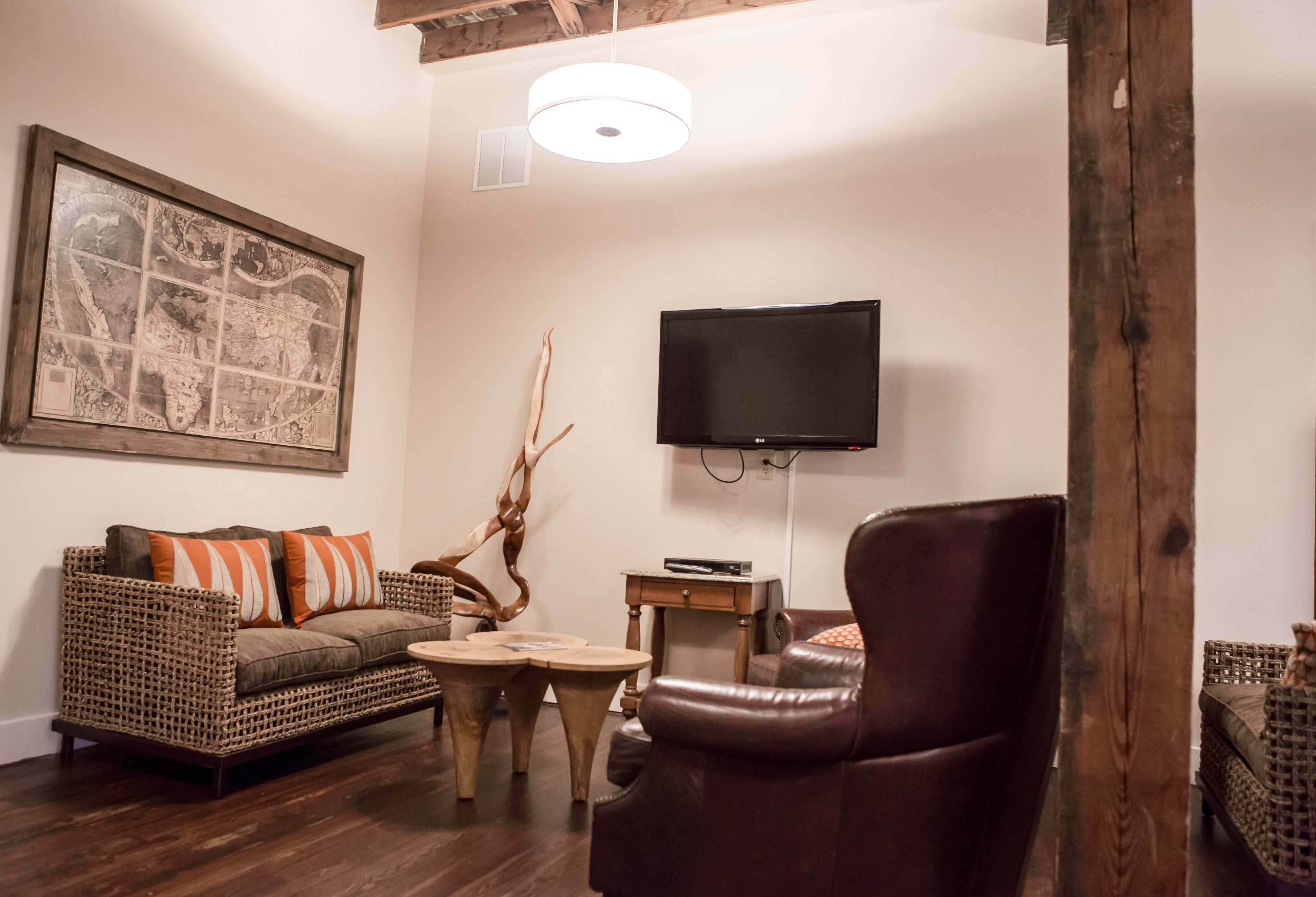 A living room with a wicker sofa, a leather armchair, a coffee table, a flat-screen TV, and a world map artwork.