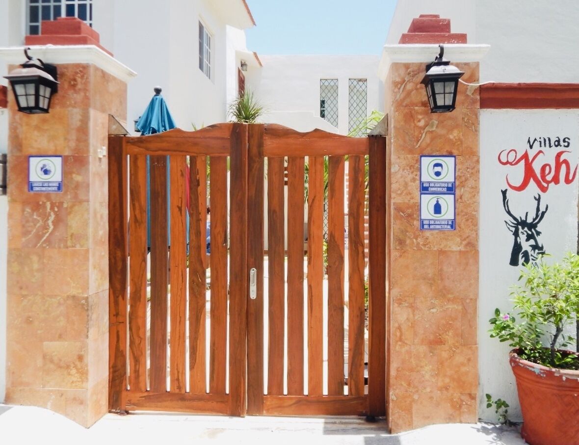 A gated entrance with a wooden gate, a potted plant, and a wall with a sign.