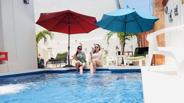 Una piscina con dos personas sentadas bajo sombrillas.