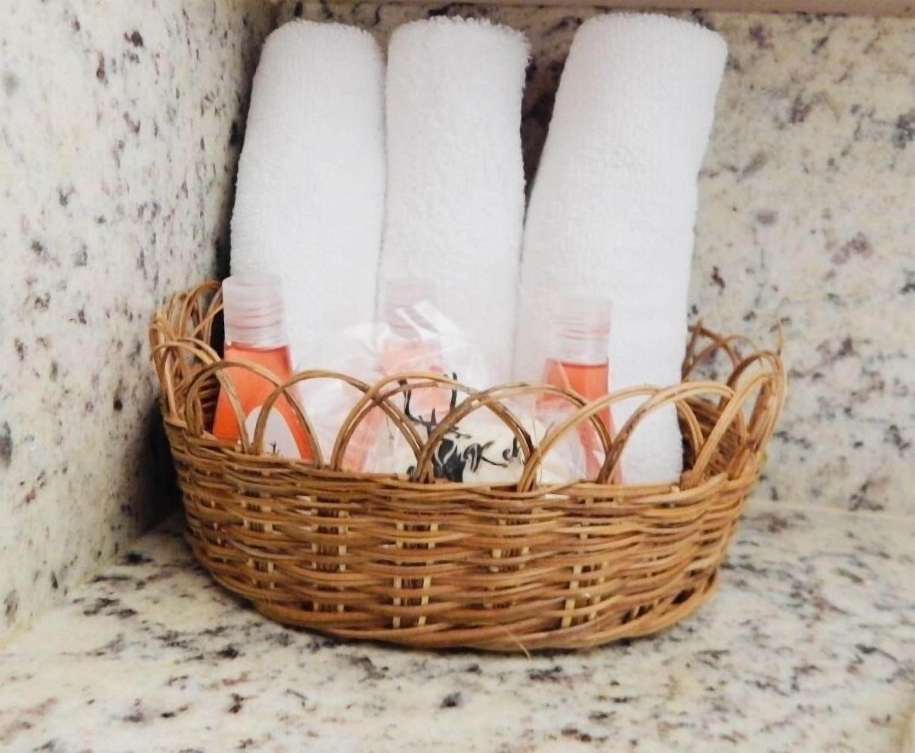 A wicker basket containing white towels and bottles of toiletries on a marble countertop.