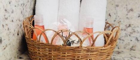 A wicker basket containing white towels and bottles of toiletries on a marble countertop.