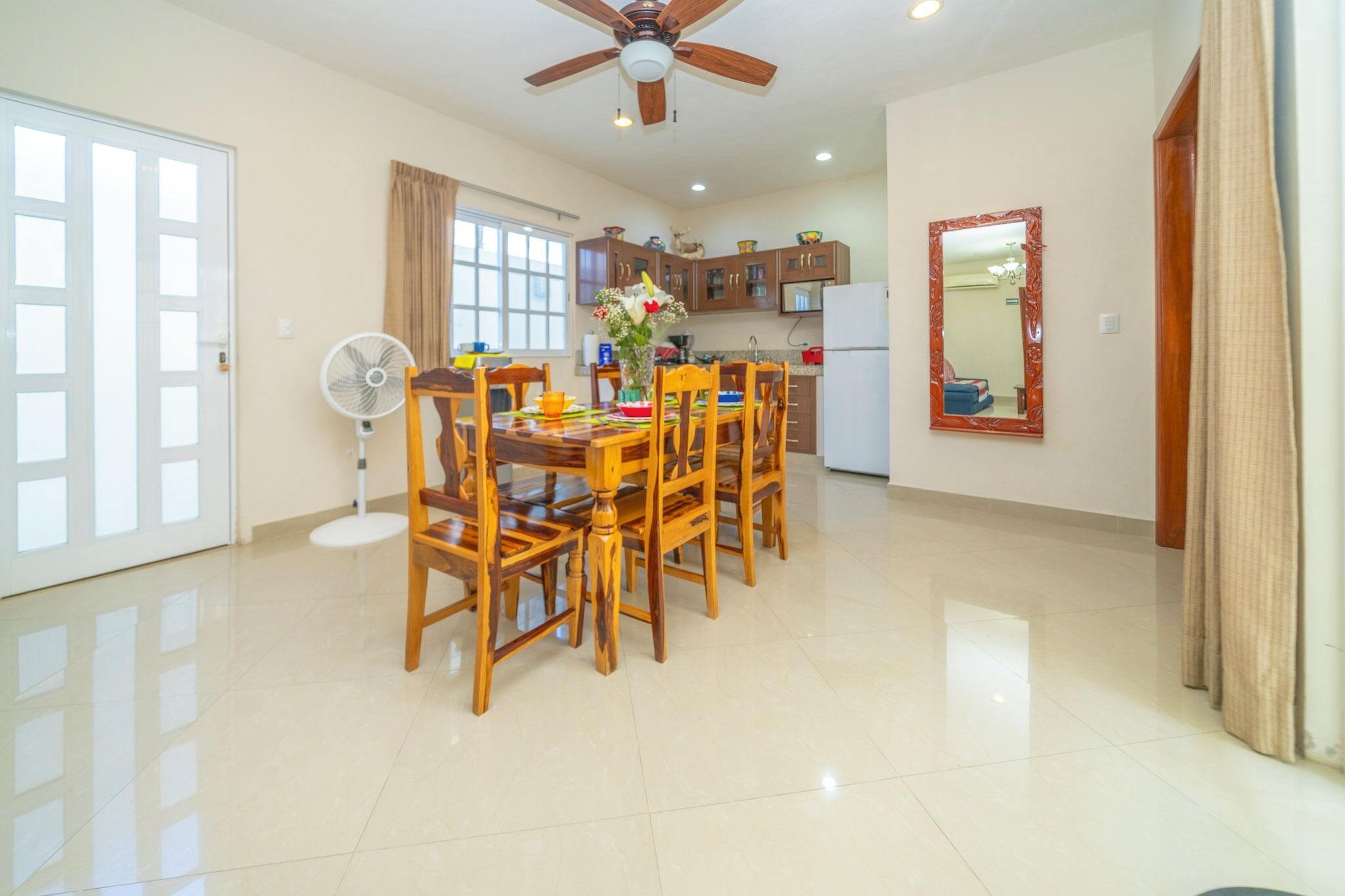 A spacious dining area with a wooden table and chairs, a ceiling fan, and a kitchen in the background.