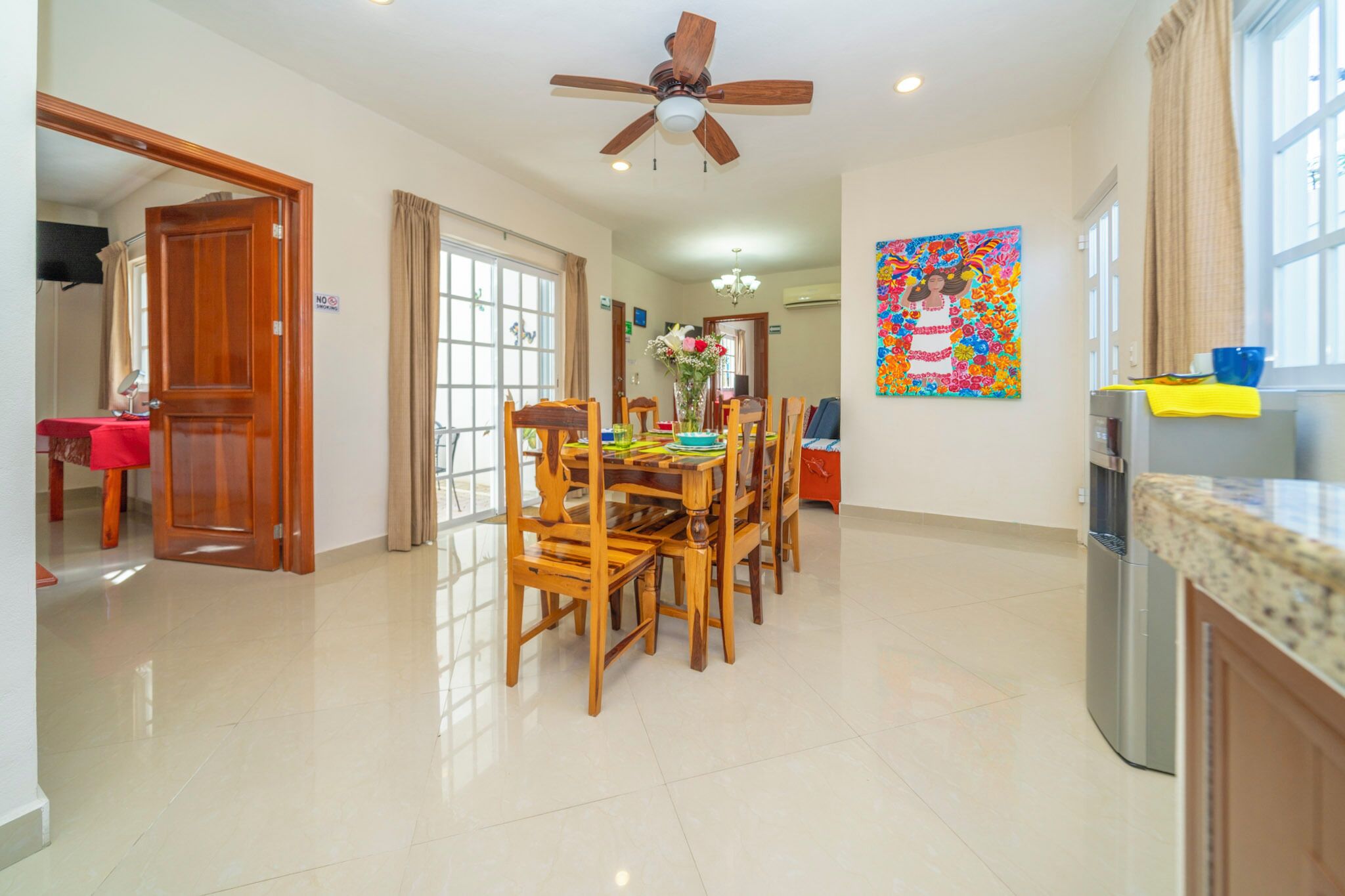 A spacious kitchen with a dining area, a ceiling fan, and a colorful painting on the wall.