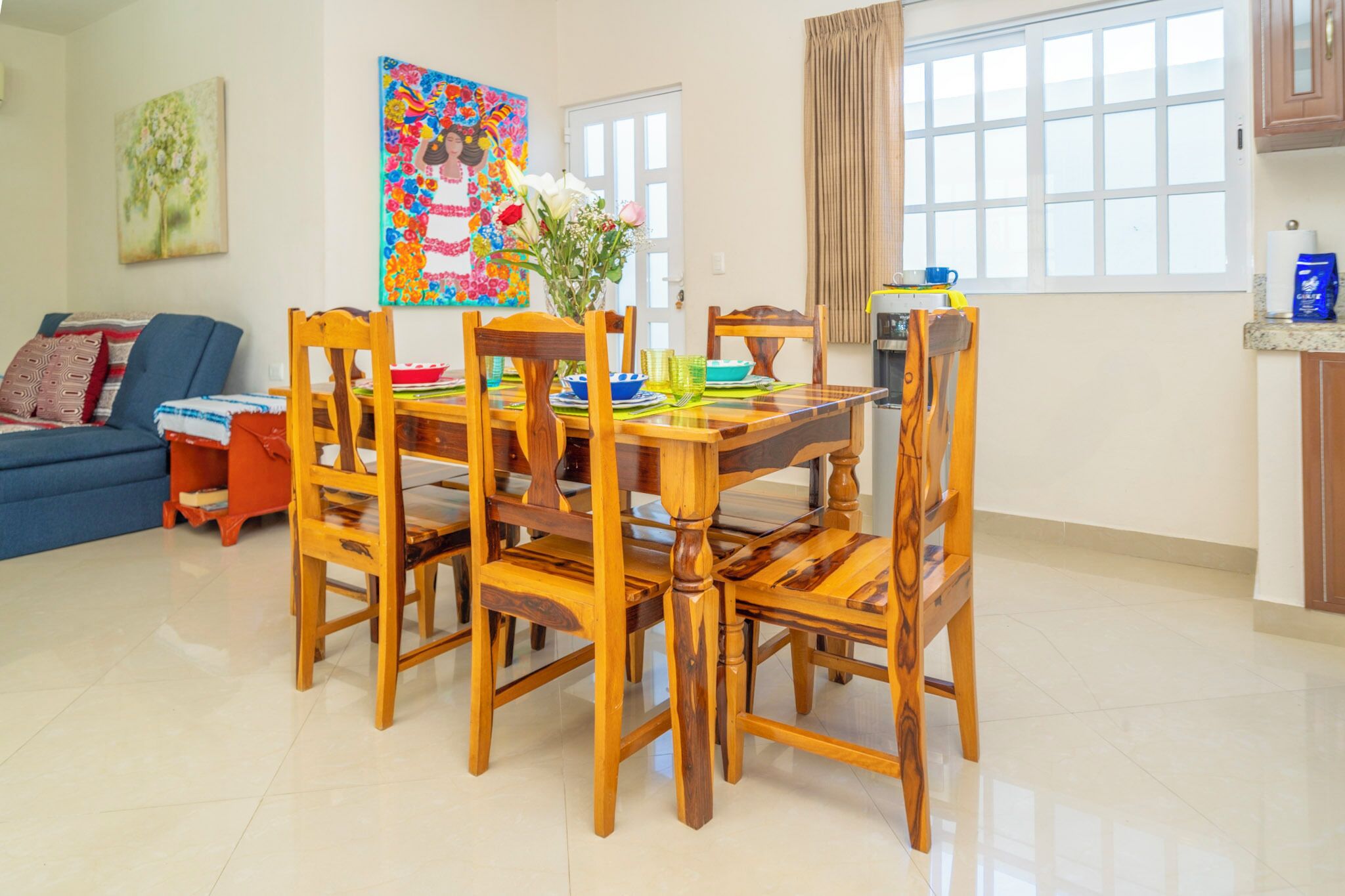 A dining area with a wooden table and chairs, a vase with flowers, and a colorful painting on the wall.