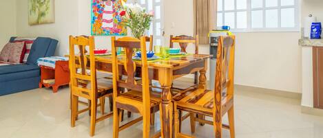 A dining area with a wooden table and chairs, a vase with flowers, and a colorful painting on the wall.