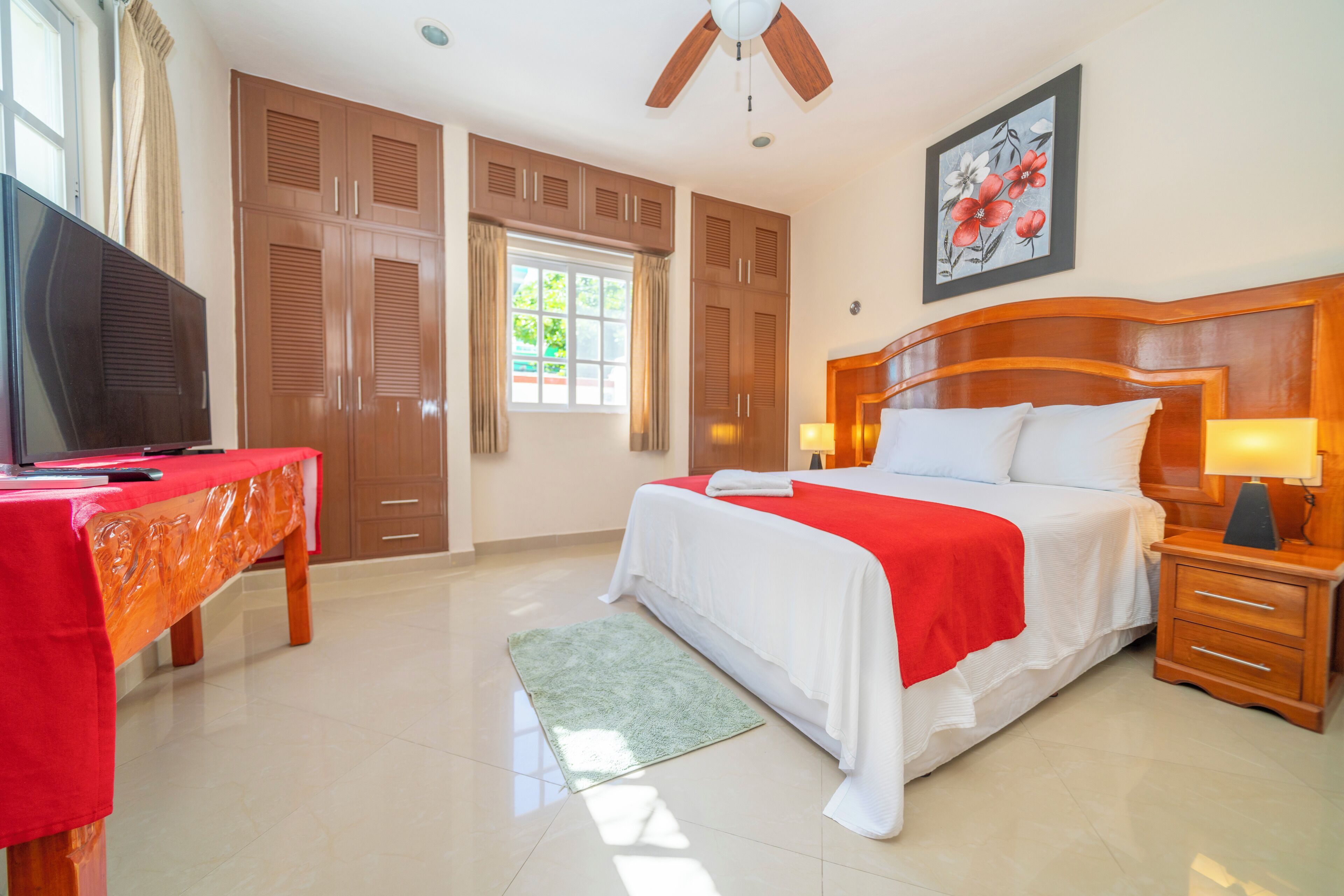 A hotel room with a bed, wooden wardrobe, a desk with a television, and a window with curtains.