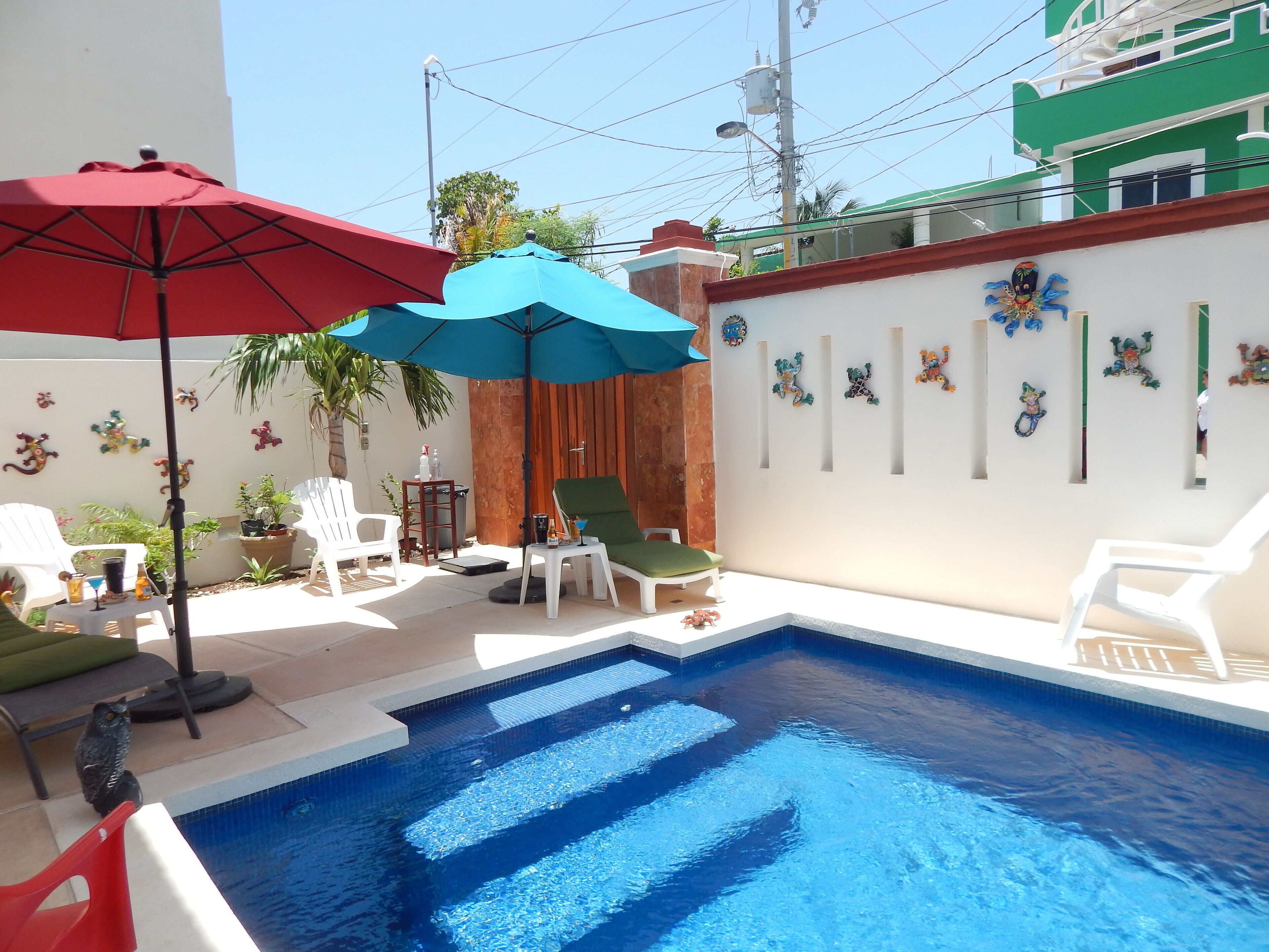 A swimming pool with two umbrellas, a chair, and a small table with drinks.