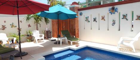 A swimming pool with two umbrellas, a chair, and a small table with drinks.