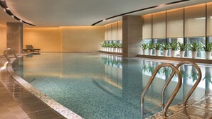 Una piscina interior moderna con agua cristalina, una escalera de metal y plantas en macetas a lo largo de las paredes.