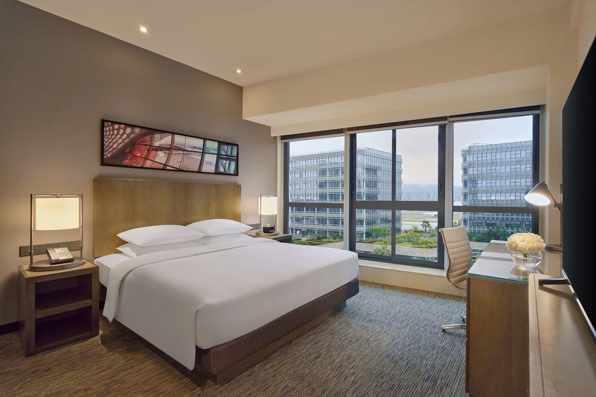 Habitación de hotel moderna con una cama grande, lámparas de noche, un escritorio con una silla y un ventanal con vistas a la ciudad.