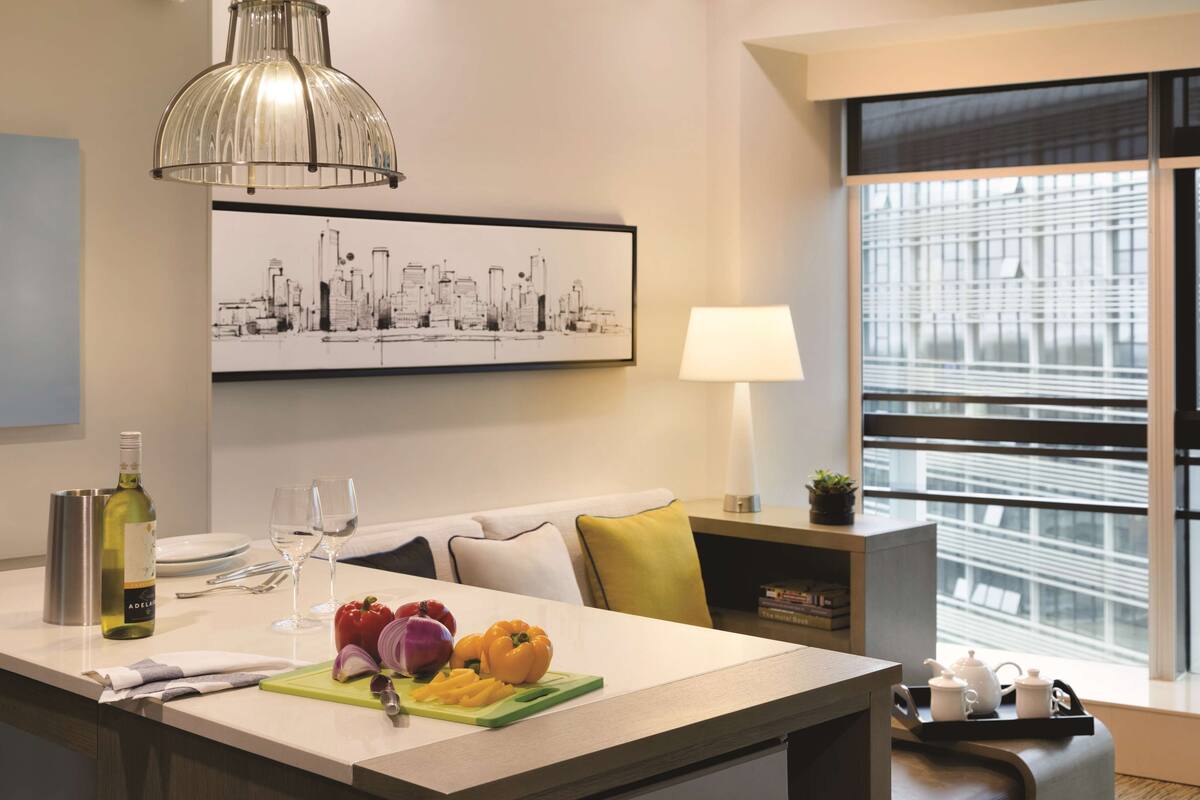 Una cocina moderna con una isla central, una obra de arte con un paisaje urbano y una ventana con persianas.