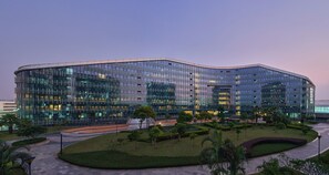 A modern glass building with a curved facade, surrounded by well-maintained landscaping and a paved walkway. - Hyatt House Shenzhen Airport (Shenzhen)