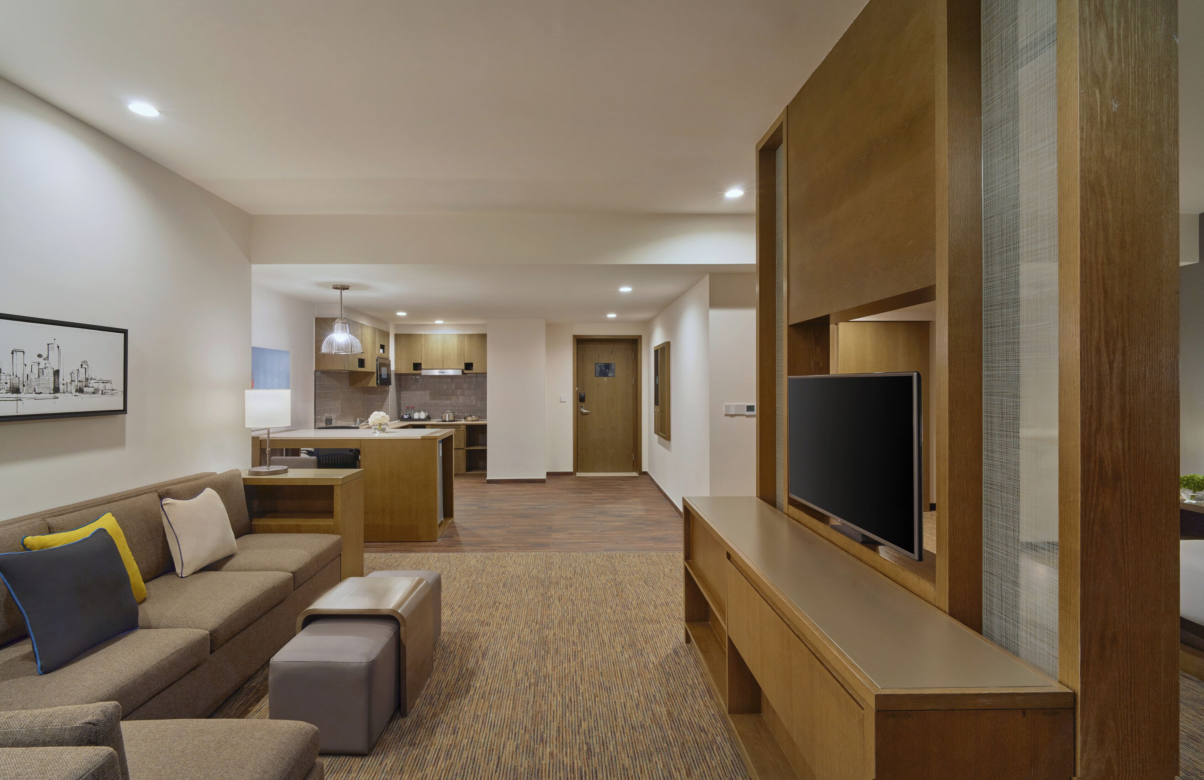 A modern hotel room with a living area, kitchenette, and a TV on a wooden stand.