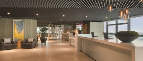 A modern reception area with a wooden floor, a reception desk, seating area with sofas, and a large window offering a view.