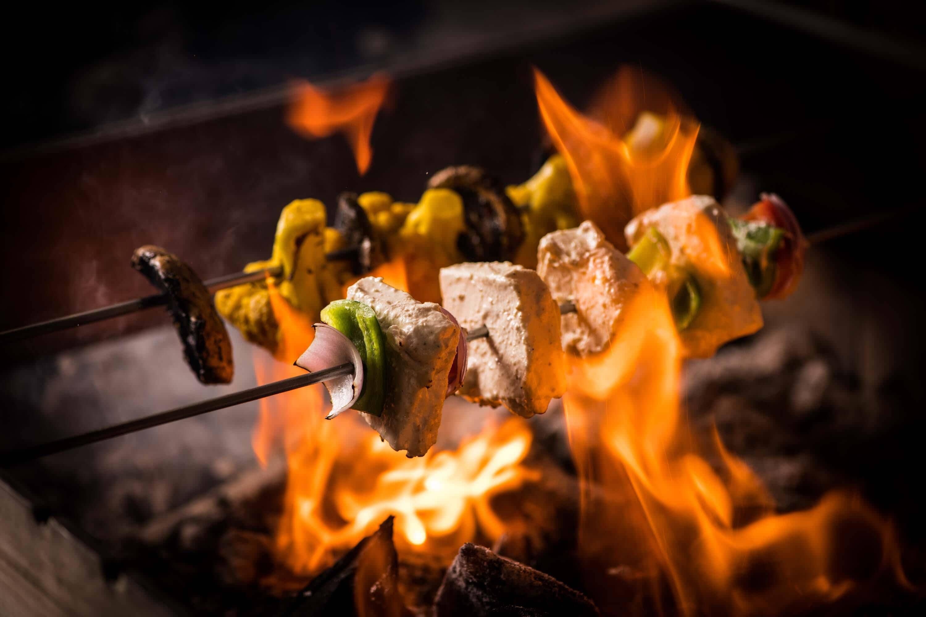 Des brochettes d’aliments sont grillées sur une flamme nue.