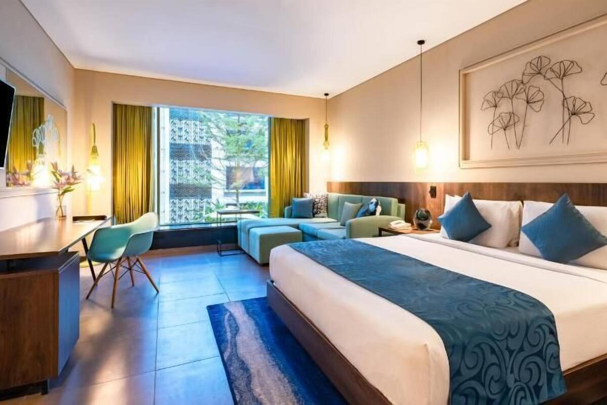 Quarto de hotel com cama, escrivaninha, cadeira, sofá e televisão.