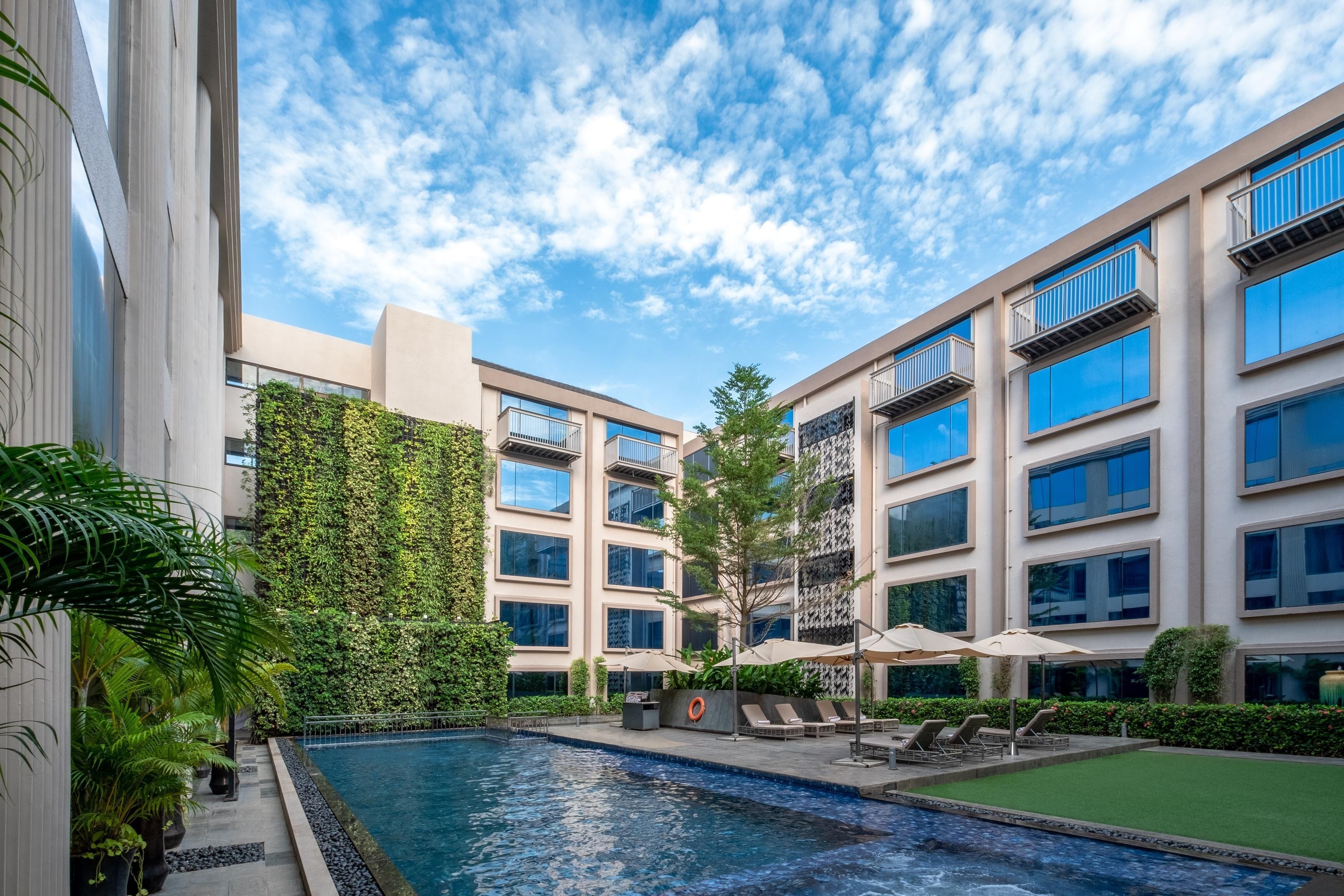 A modern building with a swimming pool, outdoor seating, and a green wall.