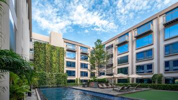 A modern building with a swimming pool, outdoor seating, and a green wall.